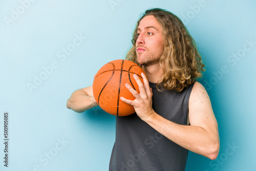 Young caucasian man playing basketball isolated on blue background