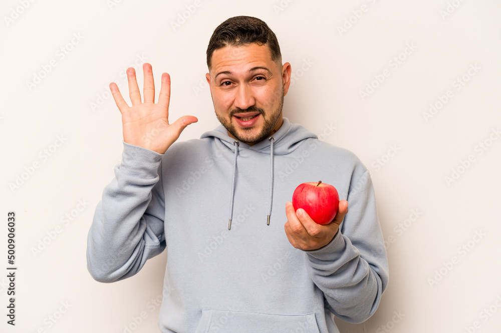 Hispanic man holding an apple isolated on white background smiling cheerful showing number five with fingers. Hispanic man holding an apple isolated on white background smiling cheerful showing number five with fingers.