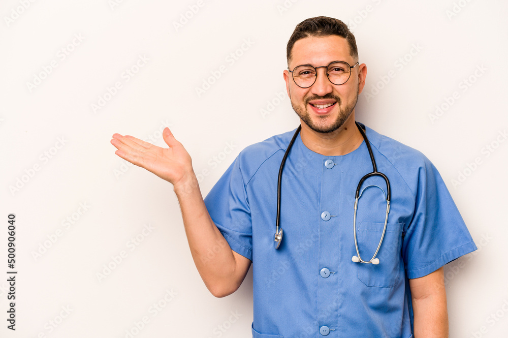 Hispanic nurse man isolated on white background showing a copy space on a palm and holding another hand on waist. Hispanic nurse man isolated on white background showing a copy space on a palm and holding another hand on waist.