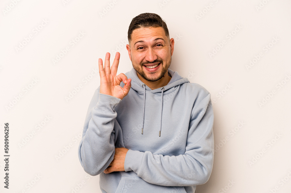 Young hispanic man isolated on white background winks an eye and holds an okay gesture with hand. Young hispanic man isolated on white background winks an eye and holds an okay gesture with hand.