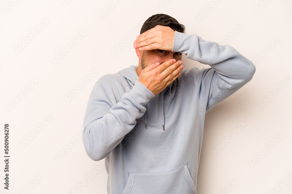 Young hispanic man isolated on white background blink at the camera through fingers, embarrassed covering face. Young hispanic man isolated on white background blink at the camera through fingers, embarrassed covering face.