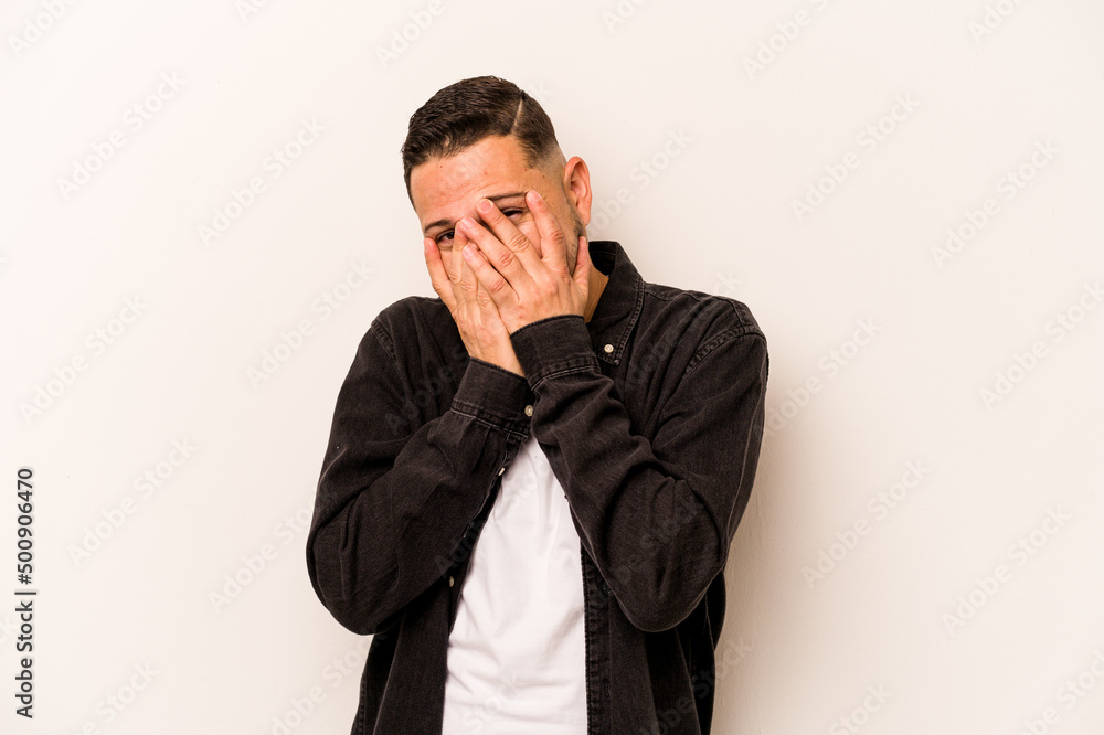 Young hispanic man isolated on white background blink at the camera through fingers, embarrassed covering face. Young hispanic man isolated on white background blink at the camera through fingers, embarrassed covering face.