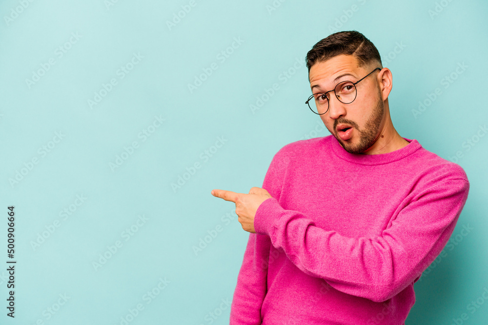 Young hispanic man isolated on blue background smiling and pointing aside, showing something at blank space. Young hispanic man isolated on blue background smiling and pointing aside, showing something at blank space.