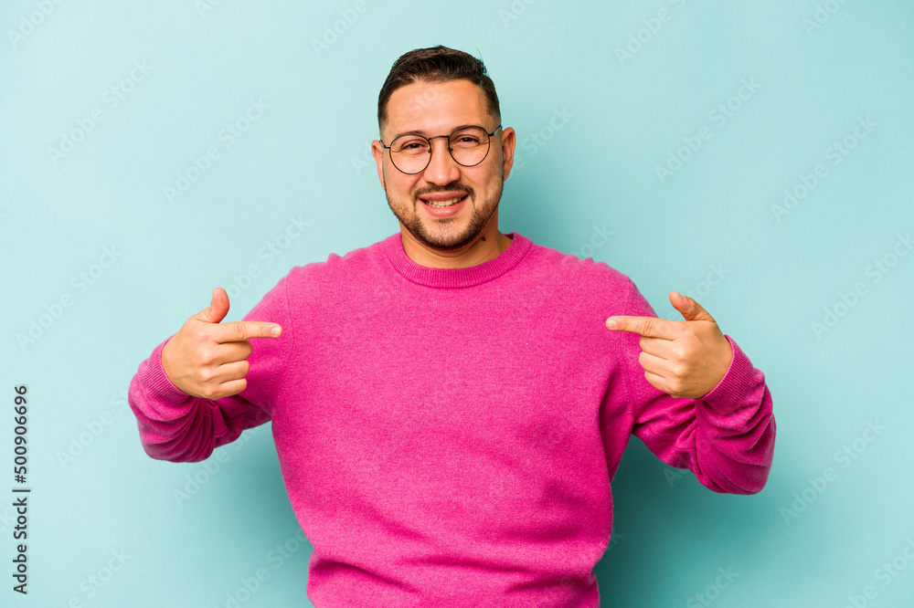 Young hispanic man isolated on blue background points down with fingers, positive feeling. Young hispanic man isolated on blue background points down with fingers, positive feeling.