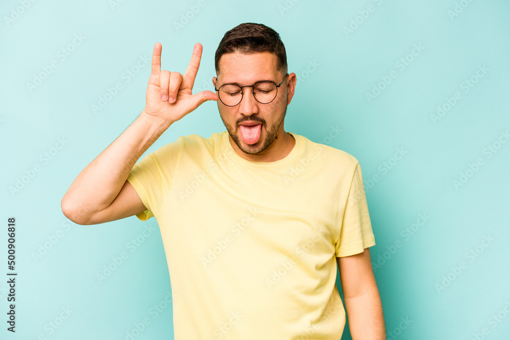 Young hispanic man isolated on blue background showing rock gesture with fingers Young hispanic man isolated on blue background showing rock gesture with fingers