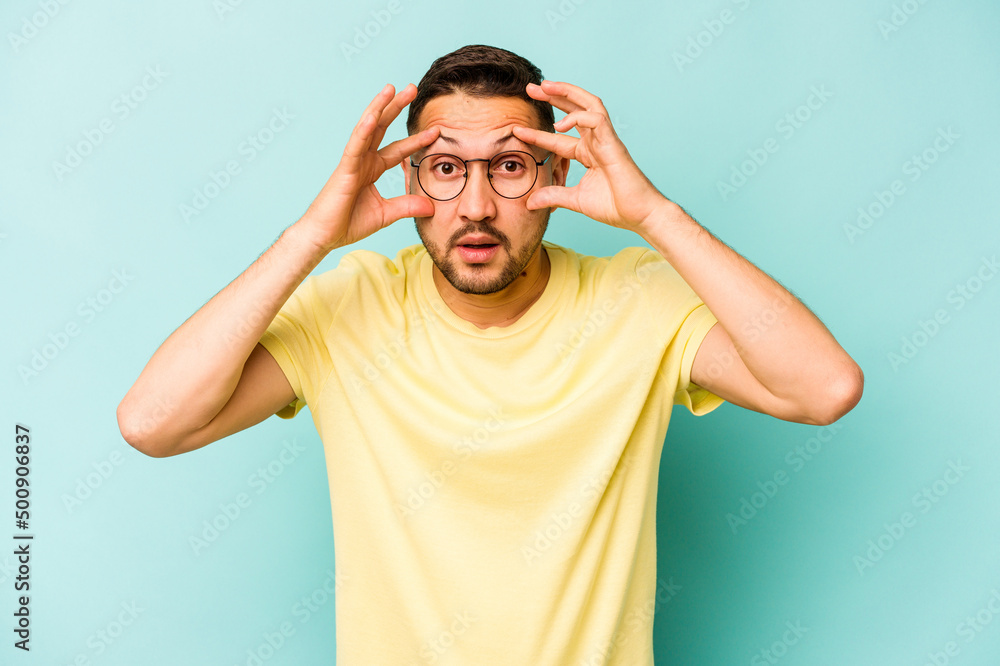 Young hispanic man isolated on blue background keeping eyes opened to find a success opportunity. Young hispanic man isolated on blue background keeping eyes opened to find a success opportunity.