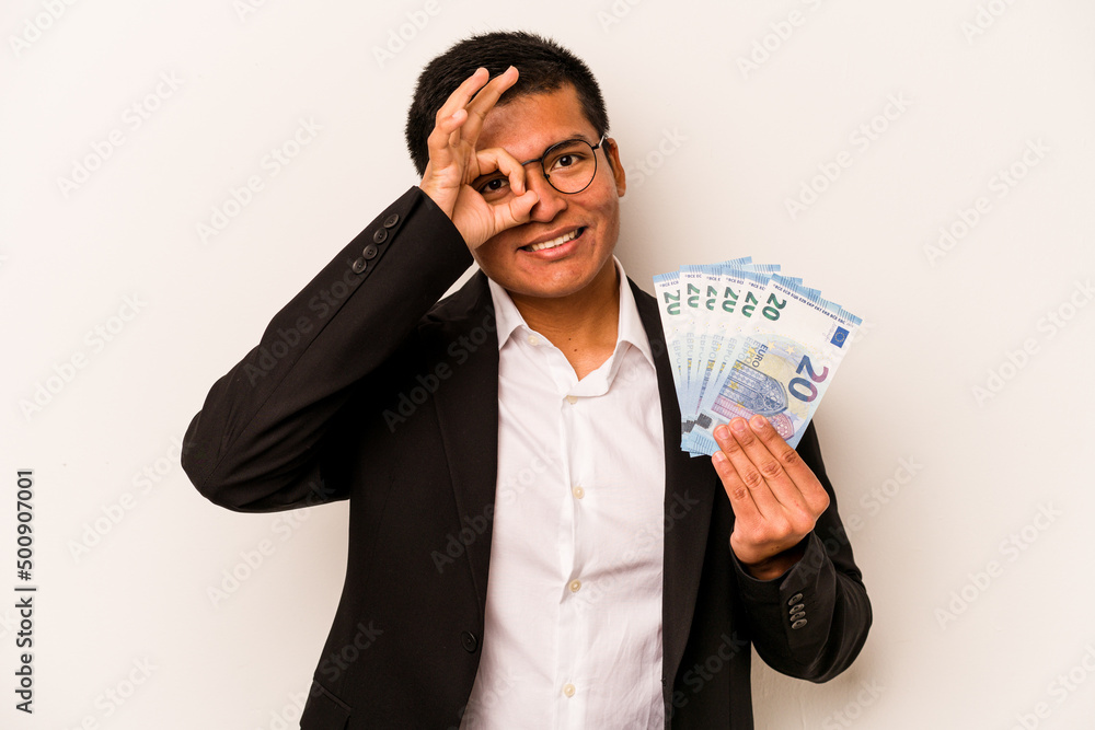 Young hispanic business man holding banknotes isolated on white background excited keeping ok gesture on eye. Young hispanic business man holding banknotes isolated on white background excited keeping ok gesture on eye.