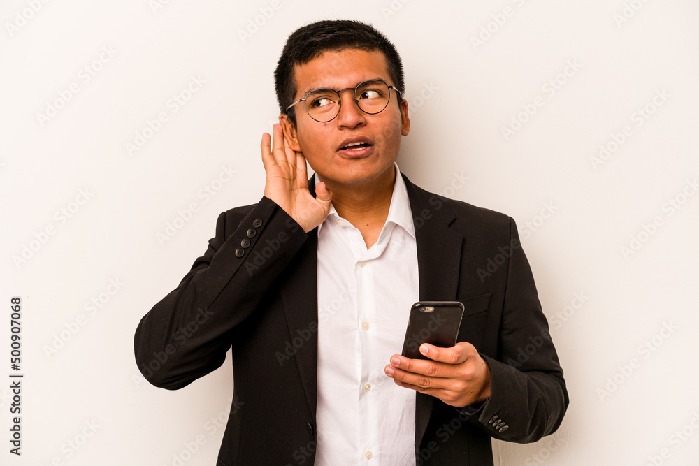 Young business hispanic man holding mobile phone isolated on white background trying to listening a gossip. Young business hispanic man holding mobile phone isolated on white background trying to listening a gossip.