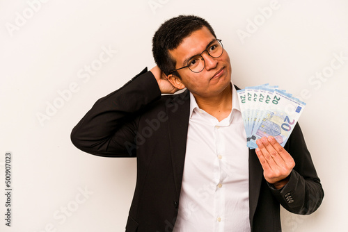 Young hispanic business man holding banknotes isolated on white background touching back of head, thinking and making a choice.