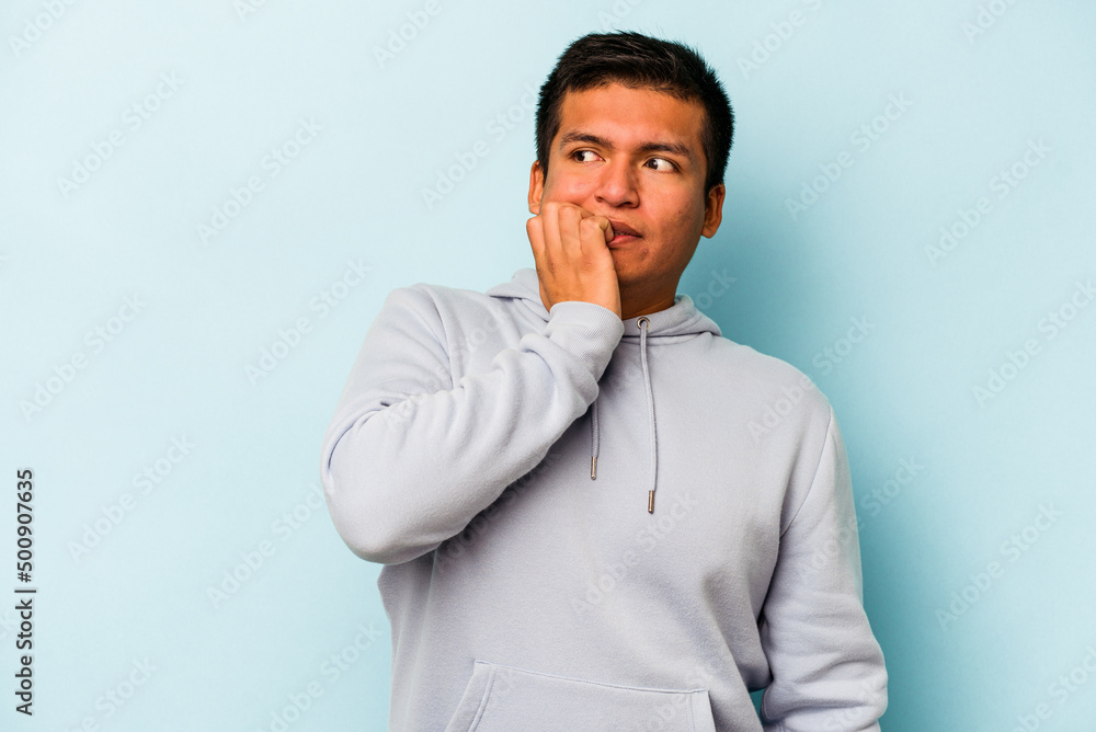 Young hispanic man isolated on blue background biting fingernails, nervous and very anxious. Young hispanic man isolated on blue background biting fingernails, nervous and very anxious.