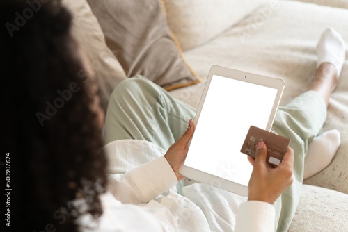 Young african american woman holding credit card and using tablet at home. Online shopping, e-commerce, internet banking