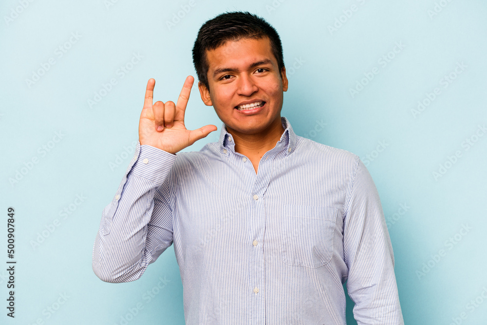 Young hispanic man isolated on blue background showing a horns gesture as a revolution concept. Young hispanic man isolated on blue background showing a horns gesture as a revolution concept.