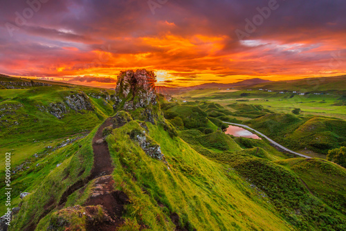 Sunset on the Isle of Skye. Landscape with rocks Castle Ewen in summer. Sandy road to rocks and hills with green grass. yellow orange red sky with clouds. Road and small lake in the background photo