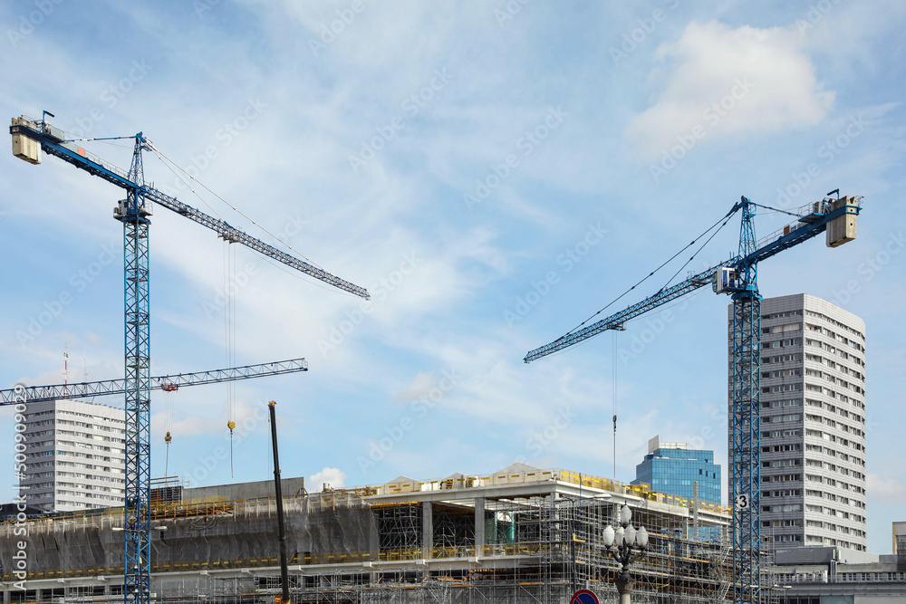 Tower cranes near unfinished building against cloudy sky Tower cranes near unfinished building against cloudy sky