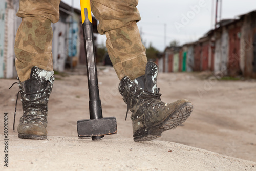 A worker with a sledgehammer, a sledgehammer and boots on the background of a warehouse.