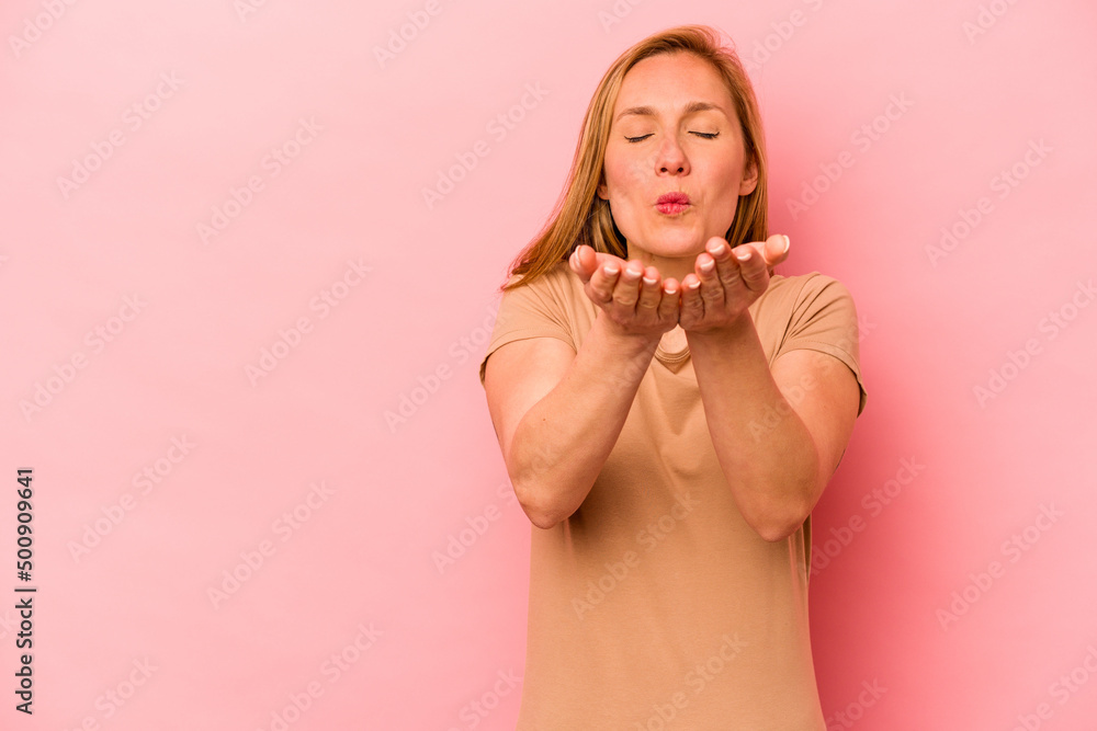Young caucasian woman isolated on pink background folding lips and holding palms to send air kiss. Young caucasian woman isolated on pink background folding lips and holding palms to send air kiss.