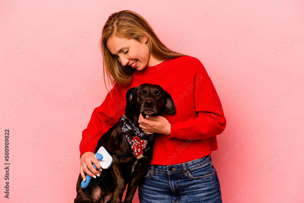 Young caucasian woman combing the dog isolated on pink background Young caucasian woman combing the dog isolated on pink background