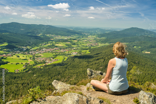 A woman sitting on mount Osser, overlooking the landscape of Lamer Winkel with the small town Lam in the Bavarian Forest