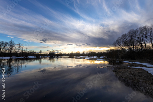 Epic spring landscape by the river. The flood of the river in early spring. A colorful sunset is reflected in the water. March evening landscape.