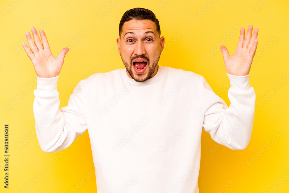 Young hispanic man isolated on yellow background celebrating a victory or success, he is surprised and shocked. Young hispanic man isolated on yellow background celebrating a victory or success, he is surprised and shocked.
