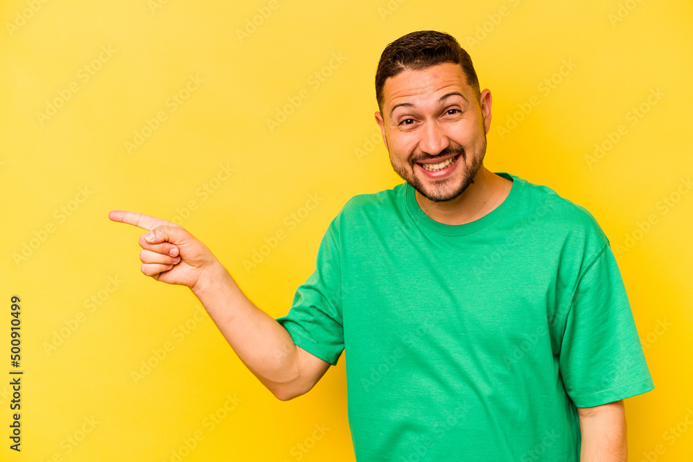 Young hispanic man isolated on yellow background smiling cheerfully pointing with forefinger away. Young hispanic man isolated on yellow background smiling cheerfully pointing with forefinger away.