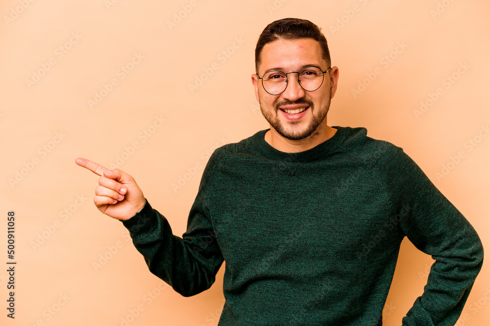Young hispanic man isolated on beige background smiling cheerfully pointing with forefinger away. Young hispanic man isolated on beige background smiling cheerfully pointing with forefinger away.