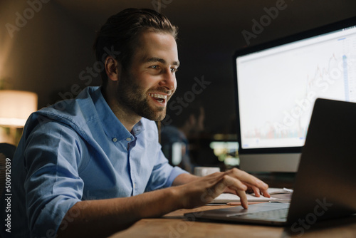 Young man working with laptop and computer while sitting at desk