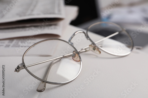 Glasses and newspapers on armrest indoors  closeup