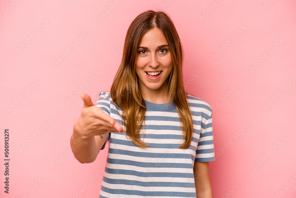 Young caucasian woman isolated on pink background stretching hand at camera in greeting gesture. Young caucasian woman isolated on pink background stretching hand at camera in greeting gesture.