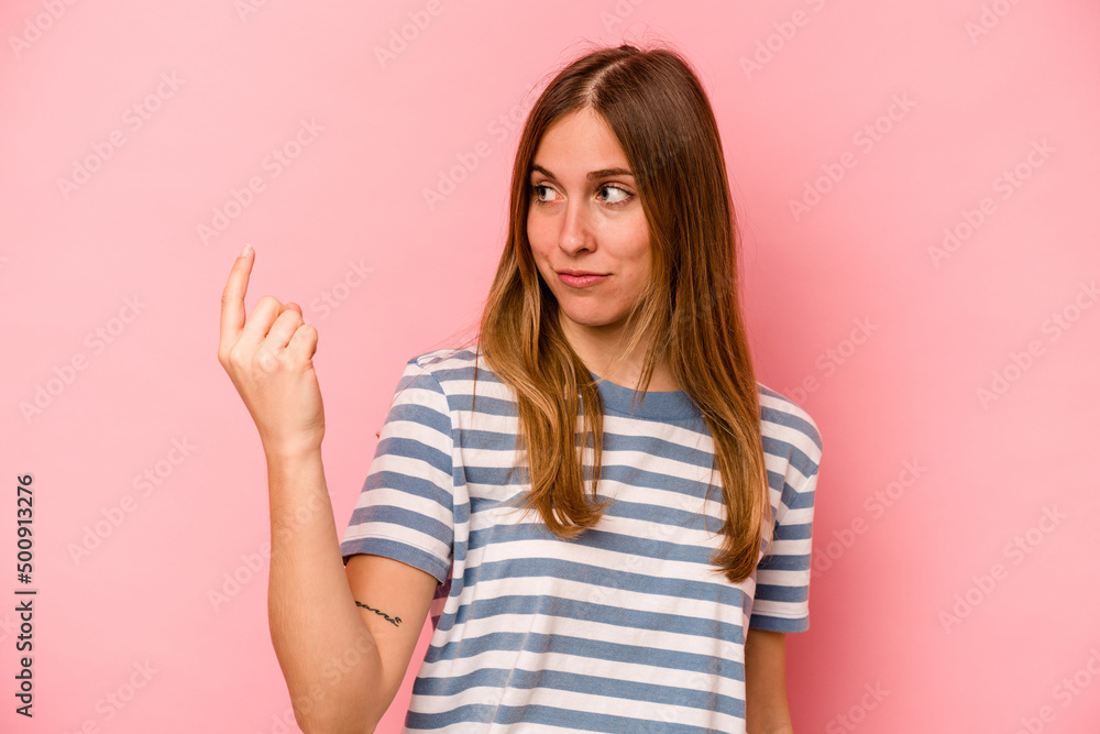 Young caucasian woman isolated on pink background pointing with finger at you as if inviting come closer. Young caucasian woman isolated on pink background pointing with finger at you as if inviting come closer.