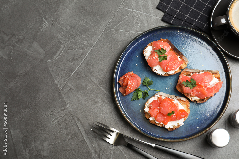Tasty bruschettas with salmon, cream cheese and parsley on grey table, flat lay. Space for text Tasty bruschettas with salmon, cream cheese and parsley on grey table, flat lay. Space for text
