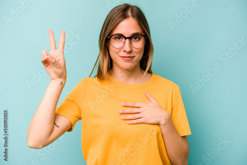 Young caucasian woman isolated on blue background taking an oath, putting hand on chest. © Asier