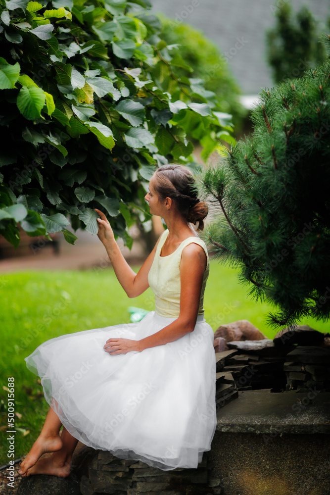 Pretty woman girl in a skirt is sitting near a small pond in a beautiful garden. Garden art and a beautiful classic lawn garden Pretty woman girl in a skirt is sitting near a small pond in a beautiful garden. Garden art and a beautiful classic lawn garden