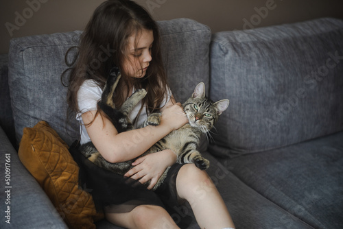 Dziecko tulące kota na szarej kanapie