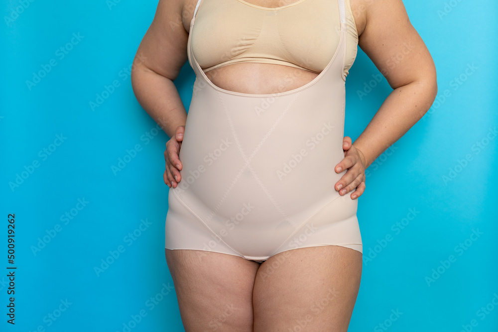 Plus size woman with cellulite hips in beige shapewear panties on belly  closeup. Tighten figure and wear lifting underwear for weight loss, blue  background. Concept of diet and fighting overweight. Photos