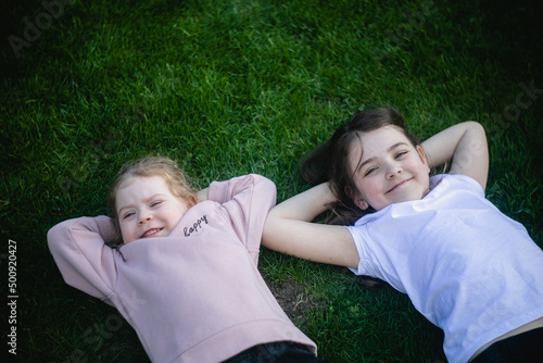 Dwie dziewczynki leżą obok siebie na plecach na zielonej trawie