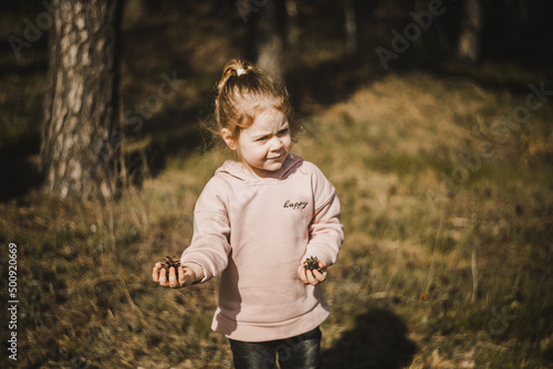 Małe dziecko trzymające w dłoni szyszki z lasu