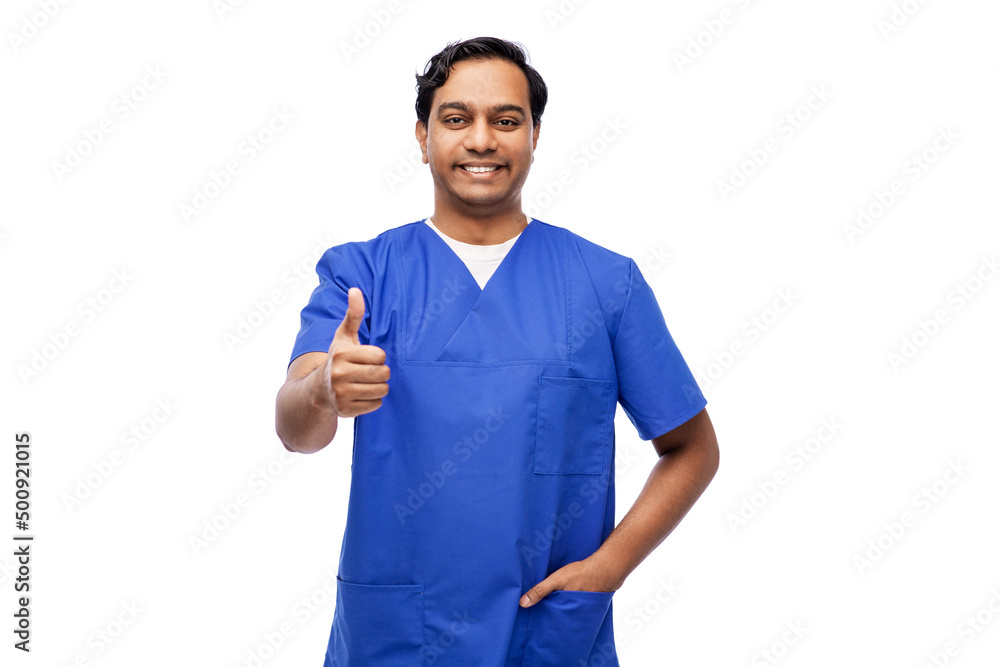 healthcare, profession and medicine concept - happy smiling indian doctor or male nurse in blue uniform showing thumbs up over white background healthcare, profession and medicine concept - happy smiling indian doctor or male nurse in blue uniform showing thumbs up over white background