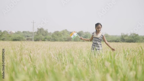 Dancing young village girl kid by holding indian flag at pady agriculture field - concept of freedom, republic or independence celebration and rural India. photo