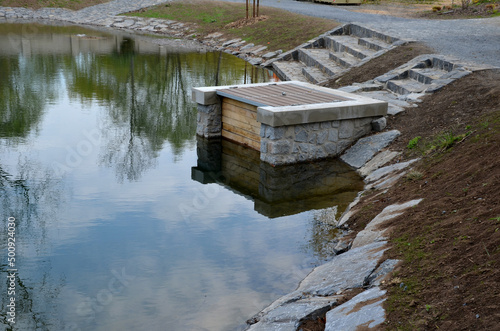 pond sluice, water reservoirs with regulation and concrete dam shaft. guide profiles determining flow, outflow under dam pipe. railing and bridge leading over water. service stone block  staircase photo