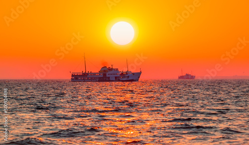 Water trail foaming behind a passenger ferry boat in the Gulf of Izmir at red sun - Izmir, Turkey