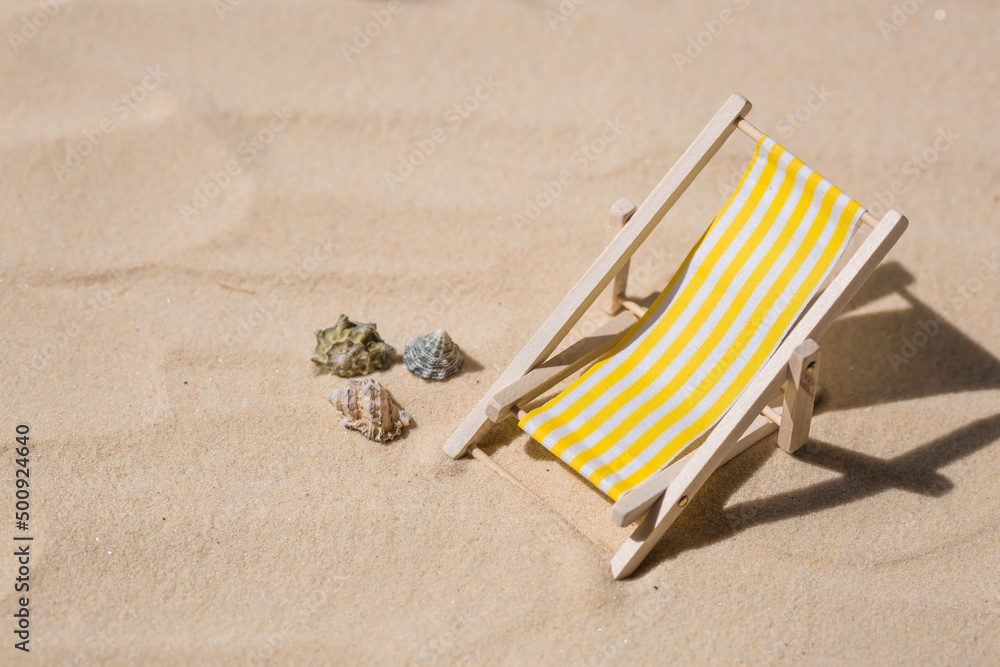 A toy beach chaise longue, seashells, a starfish on white sand with shadows. Sunlight. The concept of the sea, a beach holiday and a resort. Summer minimalism. A toy beach chaise longue, seashells, a starfish on white sand with shadows. Sunlight. The concept of the sea, a beach holiday and a resort. Summer minimalism.