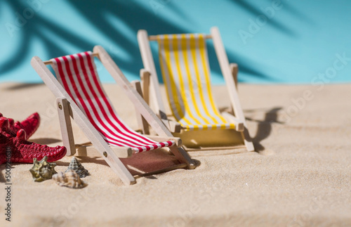 Fototapeta Naklejka Na Ścianę i Meble -  A toy beach chaise longue, seashells, a starfish on white sand with shadows. Sunlight. The concept of the sea, a beach holiday and a resort. Summer minimalism.
