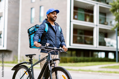 Fototapeta Naklejka Na Ścianę i Meble -  food shipping, profession and people concept - happy smiling indian delivery man with thermal insulated bag and bicycle on city street