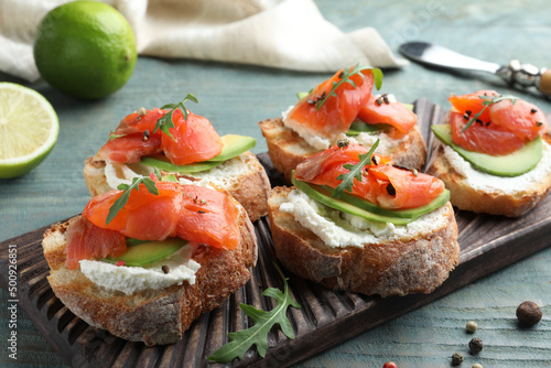 Delicious sandwiches with cream cheese, salmon, avocado and arugula on light blue wooden table, closeup