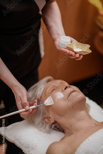 Cosmetologist applying facial revitalizing mask on a womans face