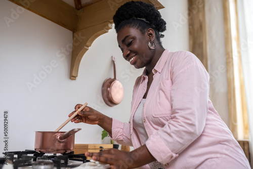 Contented african woman in pink clothes cooking in the kitchen