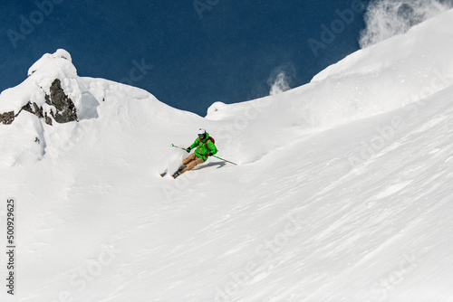freeride skier energetically rides down on snow-covered mountain slope.