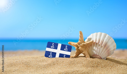 Tropical beach with seashells and Martinique flag. The concept of a paradise vacation on the beaches of Martinique. photo