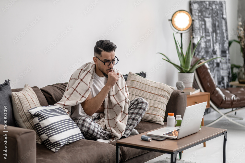 A dark-haired man feeling bad and sitting covered with a plaid A dark-haired man feeling bad and sitting covered with a plaid